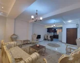مبلمان سلطنتی و فرش کرمی و سقف نورپردازی شده با نور سفید سالن نشیمن آپارتمان در عفیف آباد