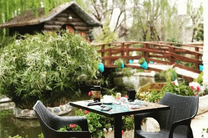 میزه وصندلی چیده شده به همراه کلبه چوبی و درختچه های سبز در کافه لاتینو شیراز 6551354 