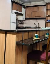 صندلی اوپن و یخچال و کابینت های قهوه ای رنگ آشپزخانه آپارتمان در قصردشت