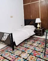 تخت خواب با روتختی سفید و عسلی و آباژور اتاق خواب آپارتمان در قصردشت